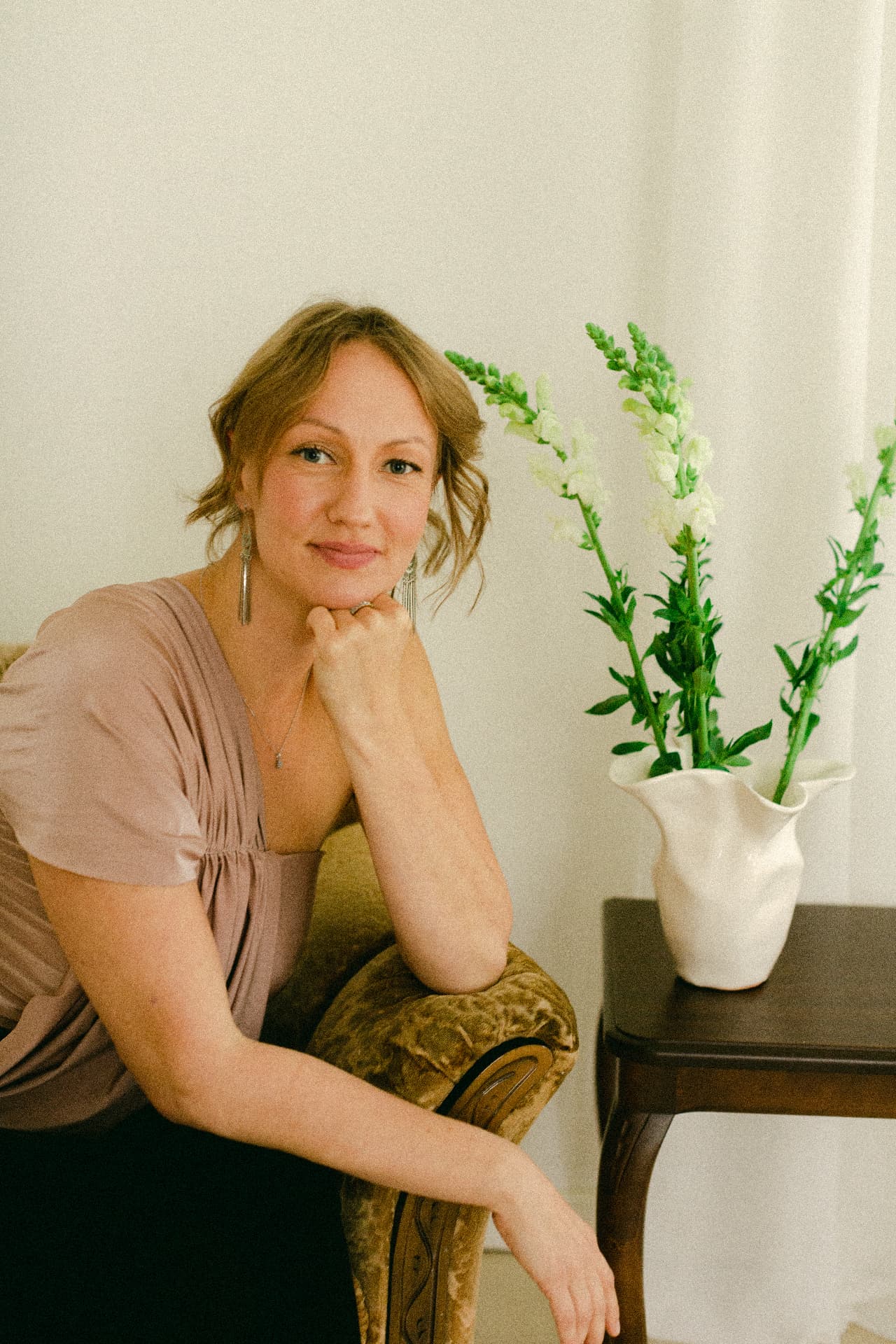 Marina Seppä seated in an armchair, chin resting lightly on her hand, smiling at the camera